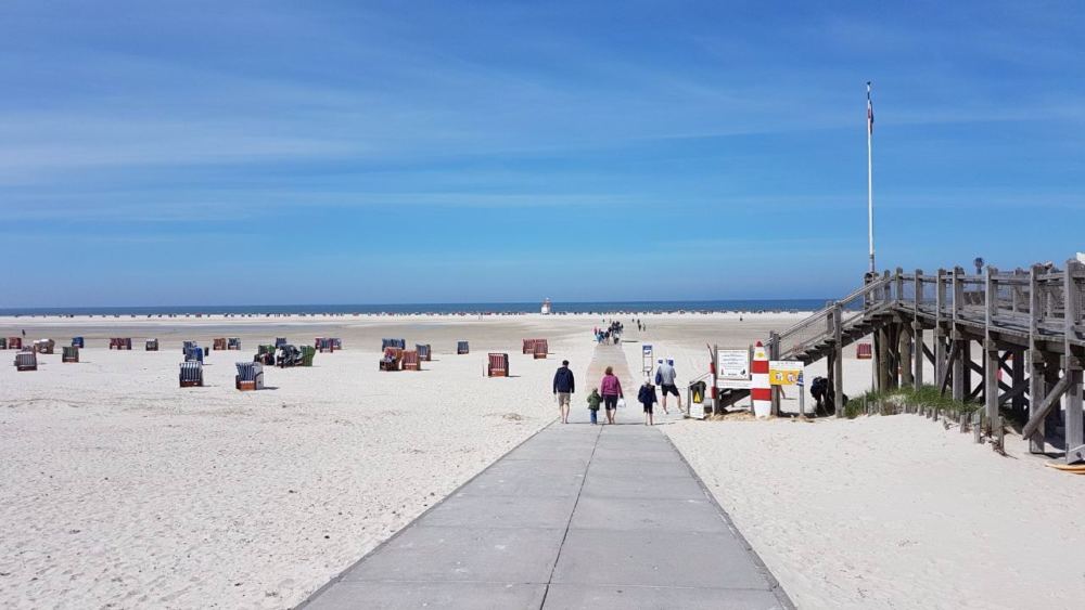 Menschen gehen auf dem Bohlenweg an den Strand in Norddorf auf Amrum.