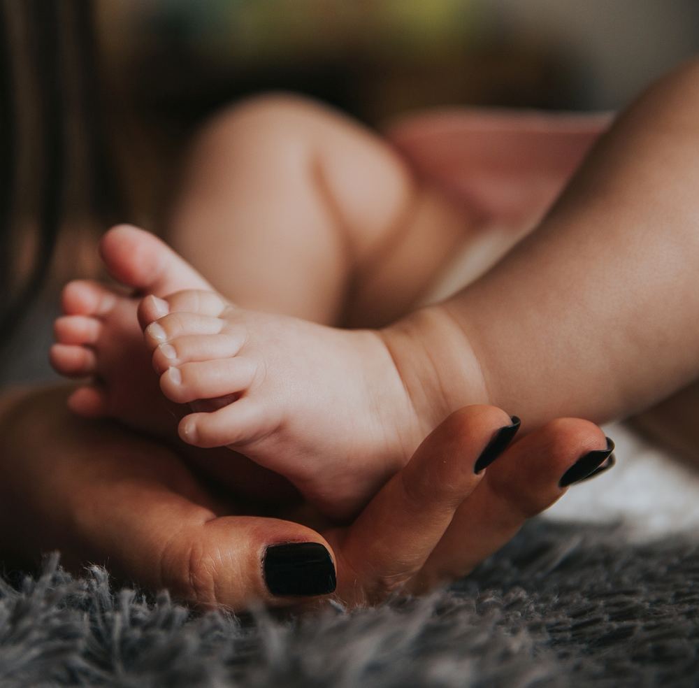 Ein Mutterhand hält zwei Babyfüße