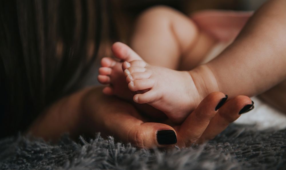Eine Mutterhand hält Babyfüße.