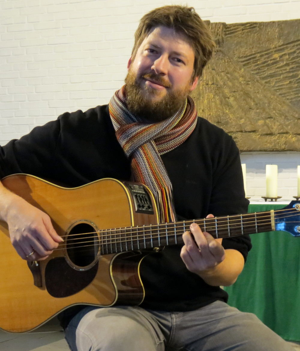 Der Popularkirchenmusiker Jan Keßler sitzt mit seiner Gitarre vor dem Altar