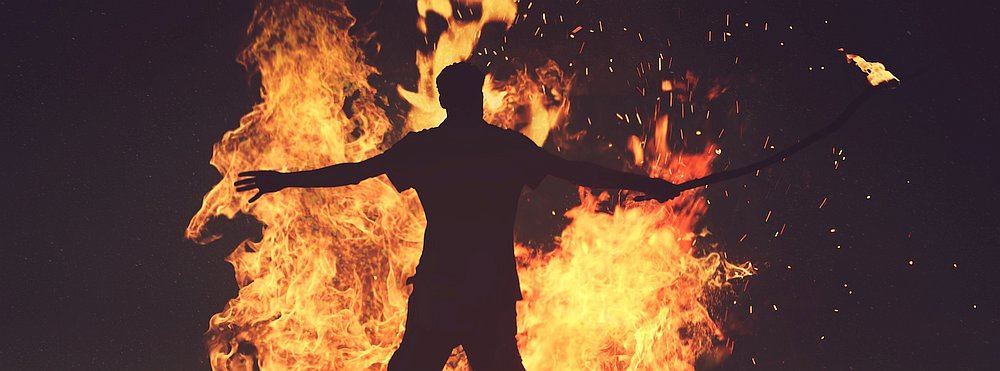 Mann steht mit ausgebreiteten Armen vor einem Feuer